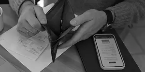 Hands holding an empty black wallet, with a smartphone and papers on a table.
