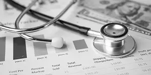 Stethoscope on financial charts and a hundred-dollar bill, illustrating medical expenses.