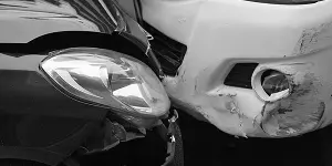 Black and white image of a black car and a white car in a collision, showing damage to both vehicles.